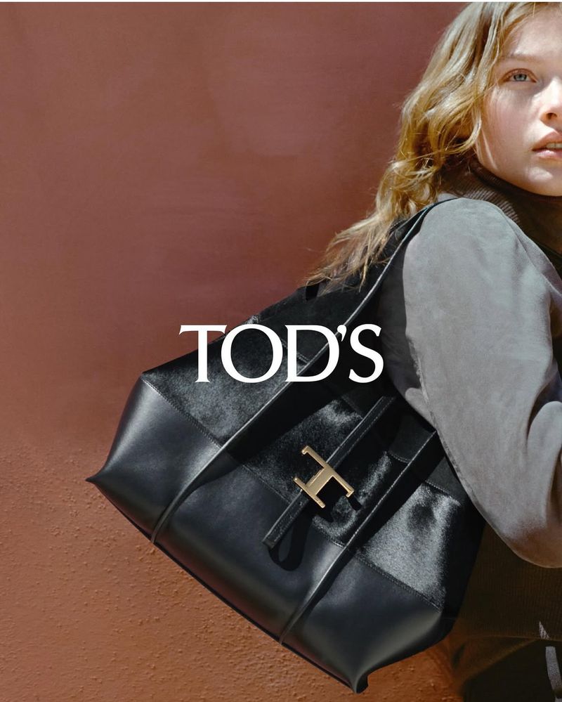 Fashion shot featuring a black Tod's handbag with a gold buckle, carried by a fair-skinned woman in soft, diffused lighting.