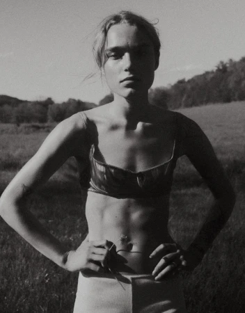 Monochrome portrait of a model in a satin bra top and light shorts standing with hands on hips in a grassy field.