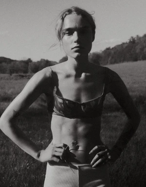 Monochrome portrait of a model in a satin bra top and light shorts standing with hands on hips in a grassy field.
