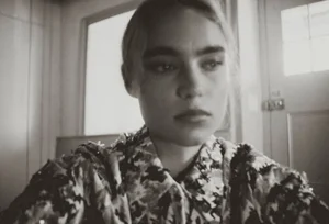 Monochrome portrait of a woman with dark eyebrows in a patterned jacket looking off-camera indoors near a windowed door.