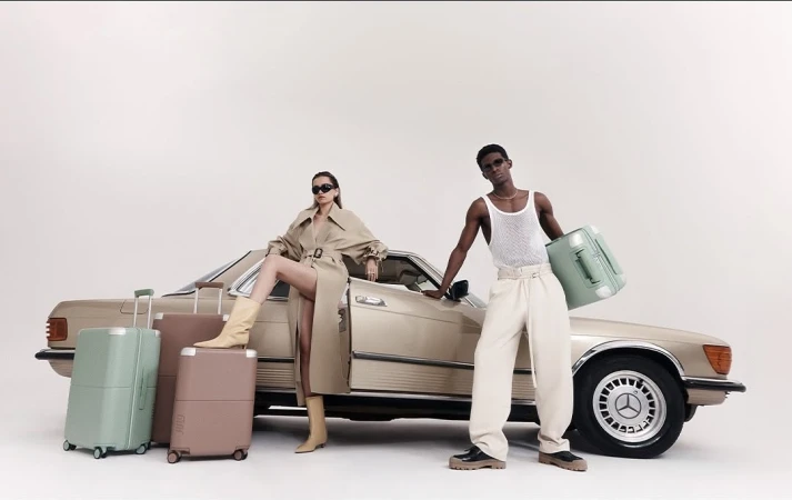 Two models posing with vintage car and matching suitcases.  A man and woman in neutral tones promote travel and fashion with matching luggage.