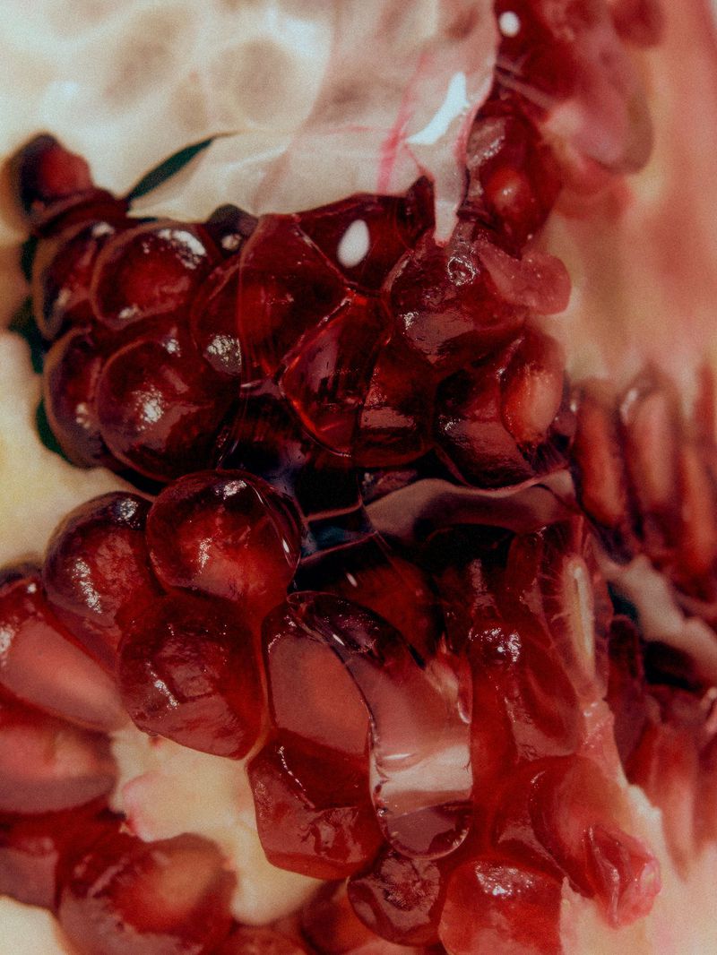 Macro close-up of glossy red pomegranate seeds nestled inside pale fruit membrane.