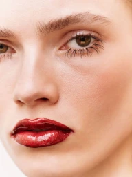 Close-up beauty portrait of a model with glossy red lips and defined dark mascara eyelashes against a neutral background.