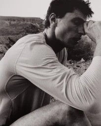 Monochrome shot of a man resting in a long-sleeve athletic performance shirt in a rocky outdoor landscape.