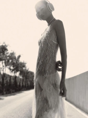 Model Xiuli Jiang wearing a textured fringe sleeveless dress and over-ear headphones standing outdoors.