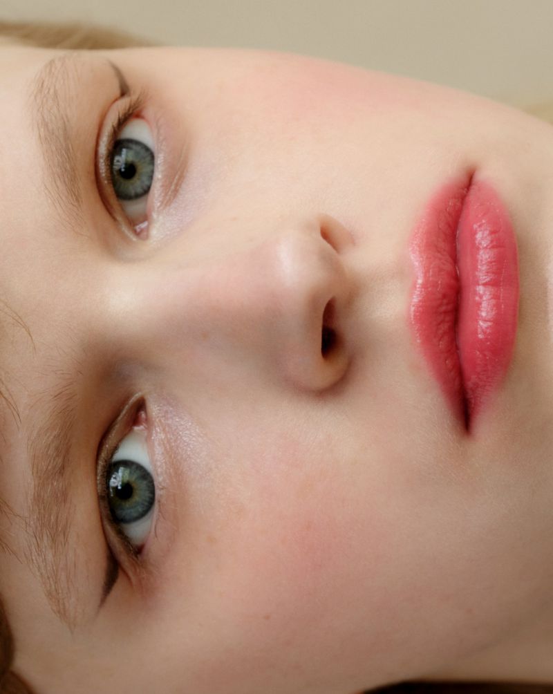 Extreme close-up beauty portrait of Hannah Motler showing blue-grey eyes and glossy pink lipstick on luminous skin.