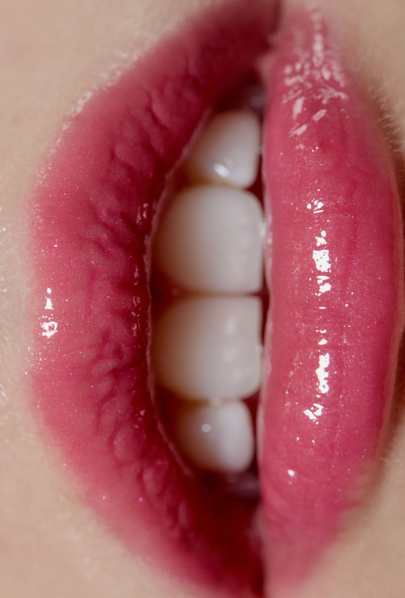 Extreme close-up of glossy pink lips parted slightly to show white teeth.