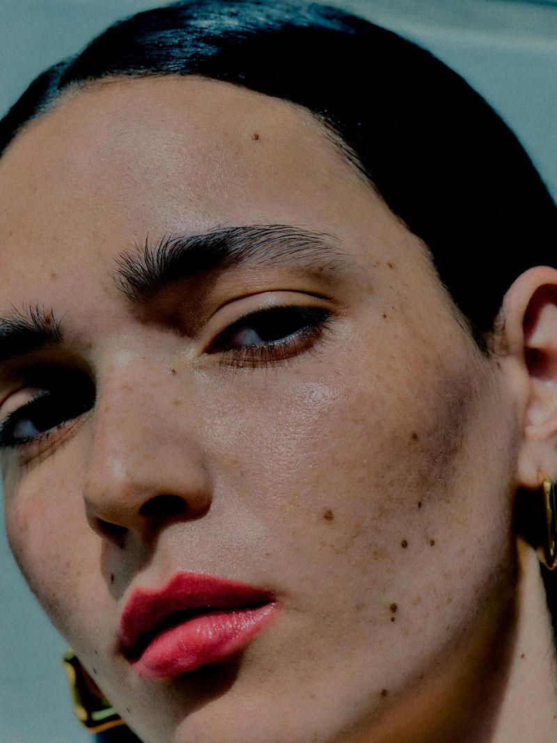 Extreme close-up beauty portrait of a woman with bold red lips, natural skin texture, and gold earrings.