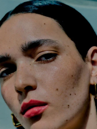 Extreme close-up beauty portrait of a woman with bold red lips, natural skin texture, and gold earrings.