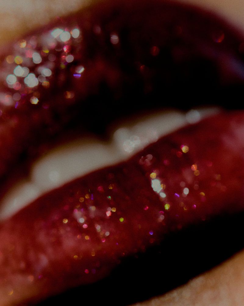 Extreme close-up of slightly parted lips coated in dark burgundy glitter lipstick.