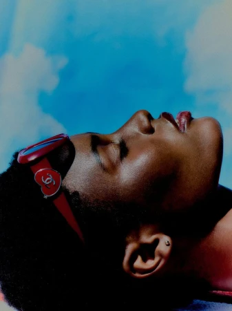 Close-up profile of a Black woman wearing red heart-accented sunglasses pushed back on her head against a blue sky.