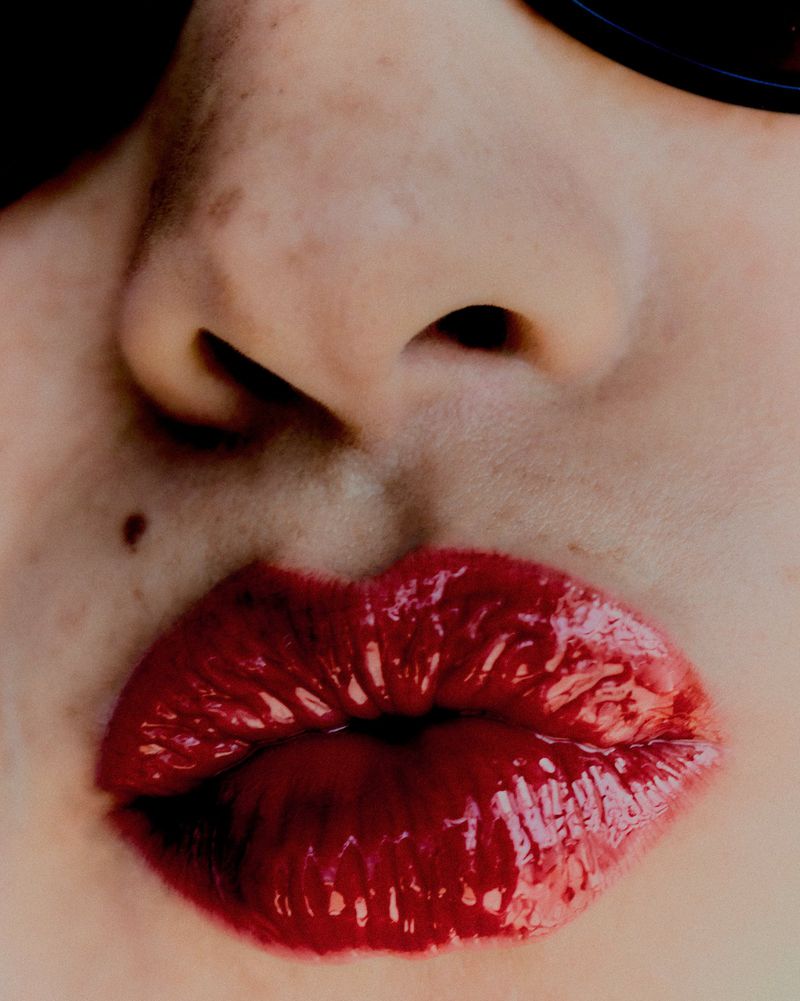 Extreme close-up of model Amaka Okafor with glossy crimson red lipstick and puckered lips.