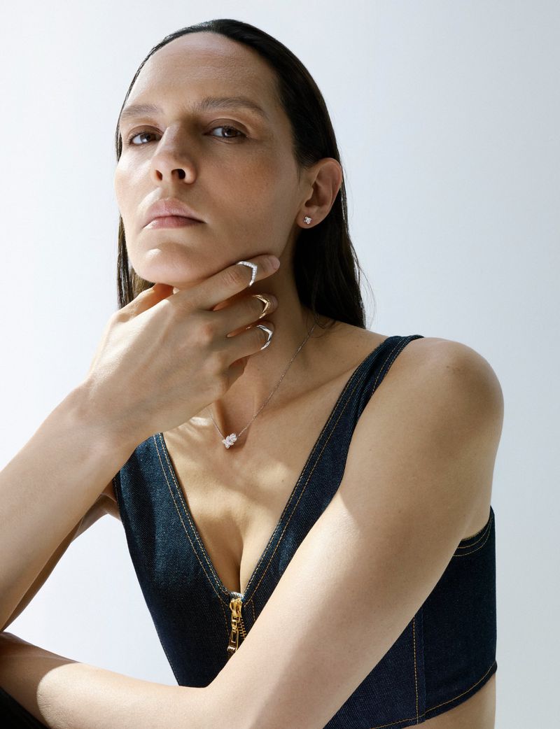 Model Laura Rylands wearing a dark denim zip-front bustier and delicate silver and gold jewelry against a white studio background.