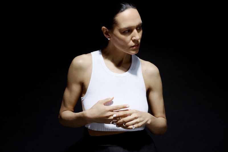 Model Laura Rylands poses in a white ribbed cropped tank top and diamond rings against a deep black background.