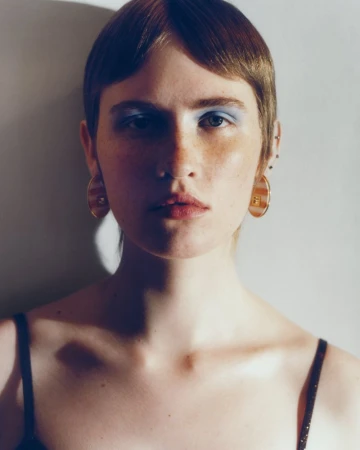 Close-up beauty portrait of a woman with short brown hair, blue eyeshadow, and striped disc earrings.