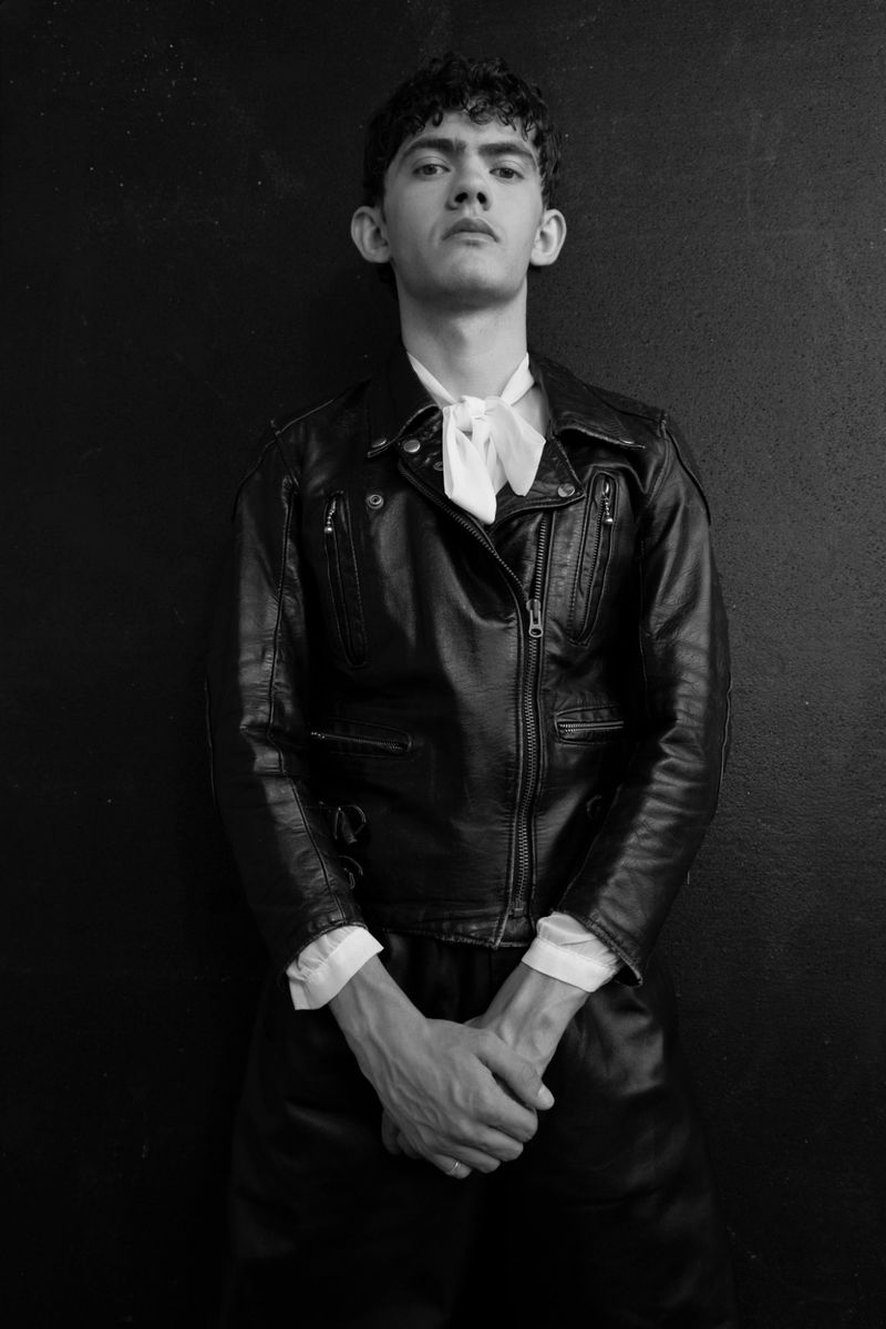 Portrait of Joe Locke wearing a black leather jacket and white necktie against a dark background for Glass Man.