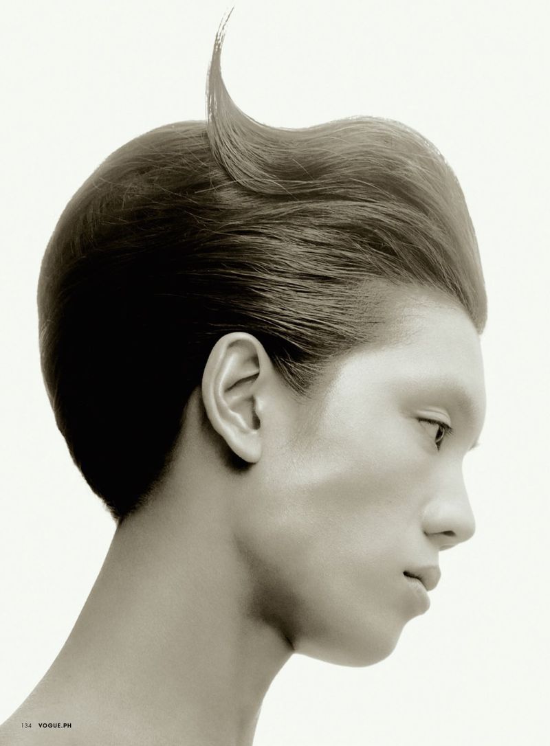 Close-up portrait showcases a young adult with light skin, a distinctive hairstyle with a front curl, and a neutral expression in a photo studio.