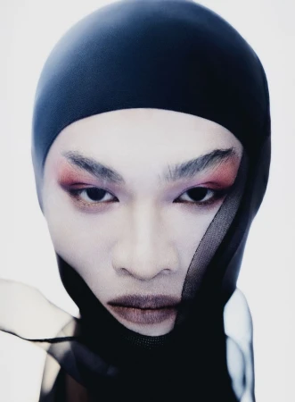 Close-up portrait of a person with artistic makeup and head covering against a white background, emphasizing bold makeup and unique style.