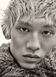 Close-up portrait of model Eden Huang with bleached wavy hair wearing a textured fur collar against a pale backdrop.