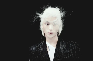 Model Eden Huang with sculptural white hair wearing a textured black blazer and white Gucci collar against a black background.