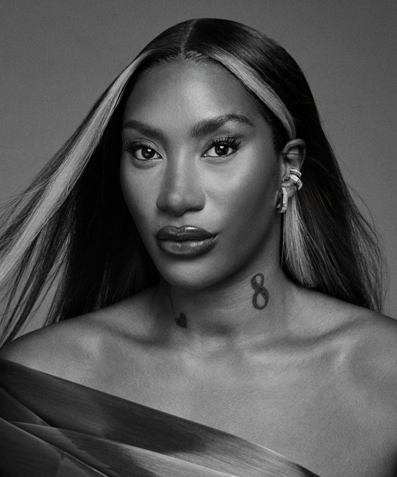 Black and white portrait of Aya Nakamura with highlighted hair and ear cuffs against a studio background.