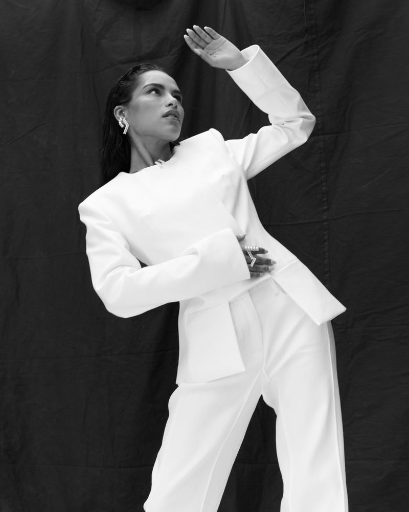 Monochrome portrait of Saffron Hocking wearing a structured white suit against a dark textured fabric backdrop.