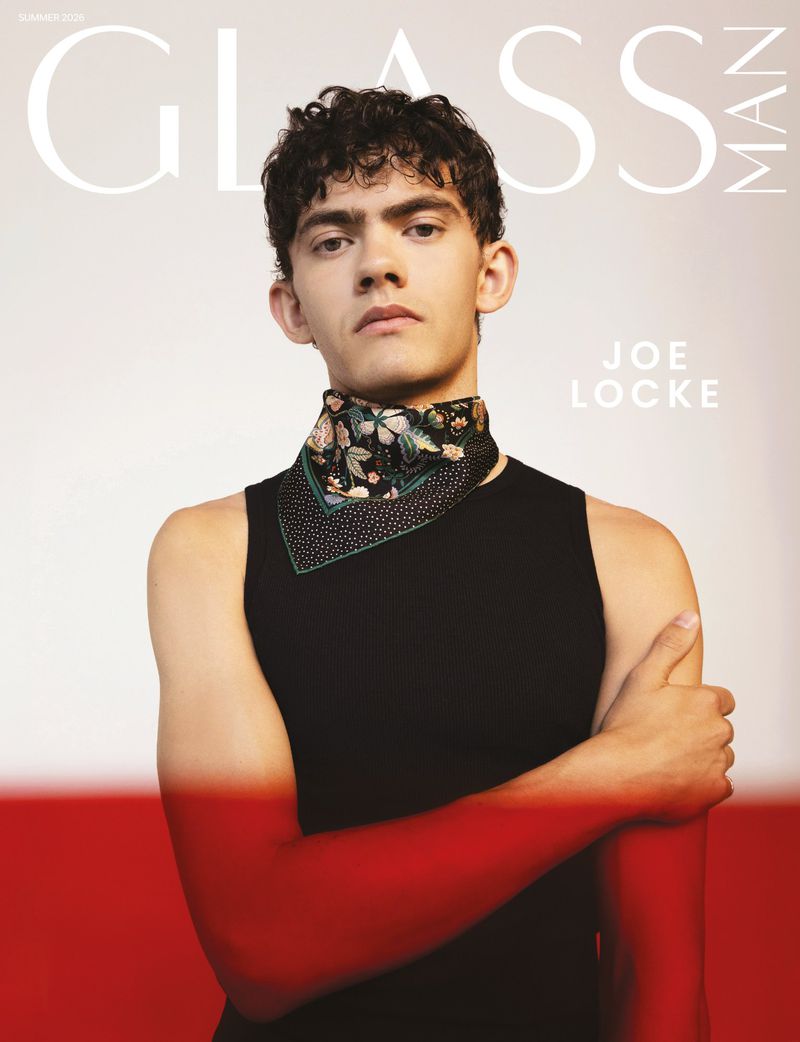 Actor Joe Locke poses for Glass Man Magazine wearing a black tank top and patterned neck scarf against a studio backdrop.