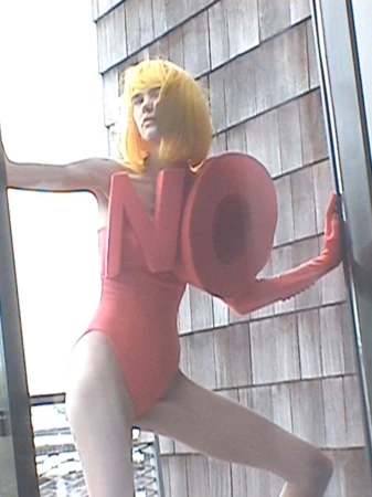 Model in red swimsuit with oversized letter letters and yellow wig posing outdoors