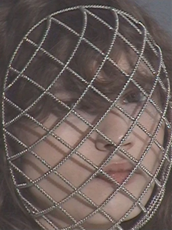 Model wearing an intricate diamond mesh silver crystal face cage over her face in a close-up editorial portrait.