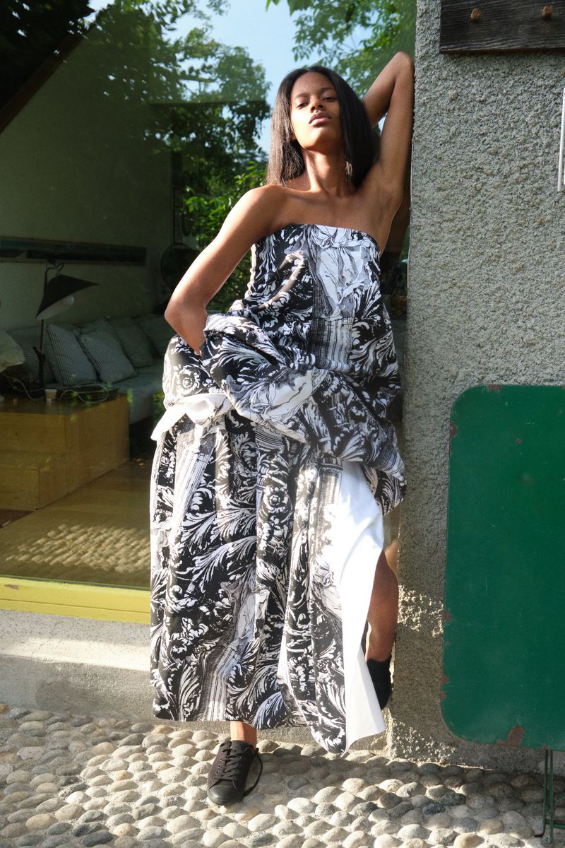 Wendy Garcia poses leaning against an exterior wall wearing a voluminous strapless black and white printed dress and black sneakers.