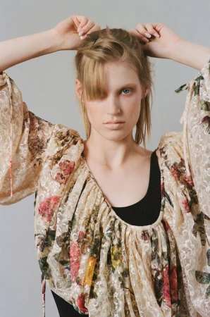 Model Jacqui Hooper poses in a voluminous floral lace blouse over a black top against a light grey studio background.