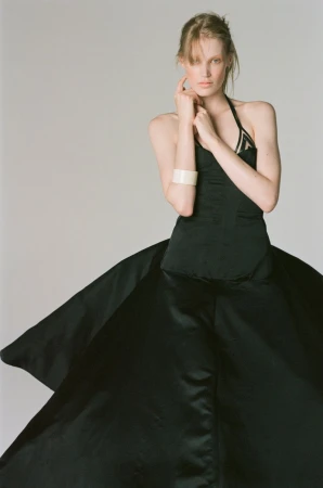 Model Jacqui Hooper wearing a voluminous black halter gown and wide white cuff bracelet against a grey backdrop.