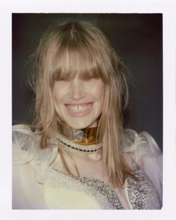 Polaroid portrait of model Jacqui Hooper smiling in a beaded choker necklace and sequined white gown against a dark background.