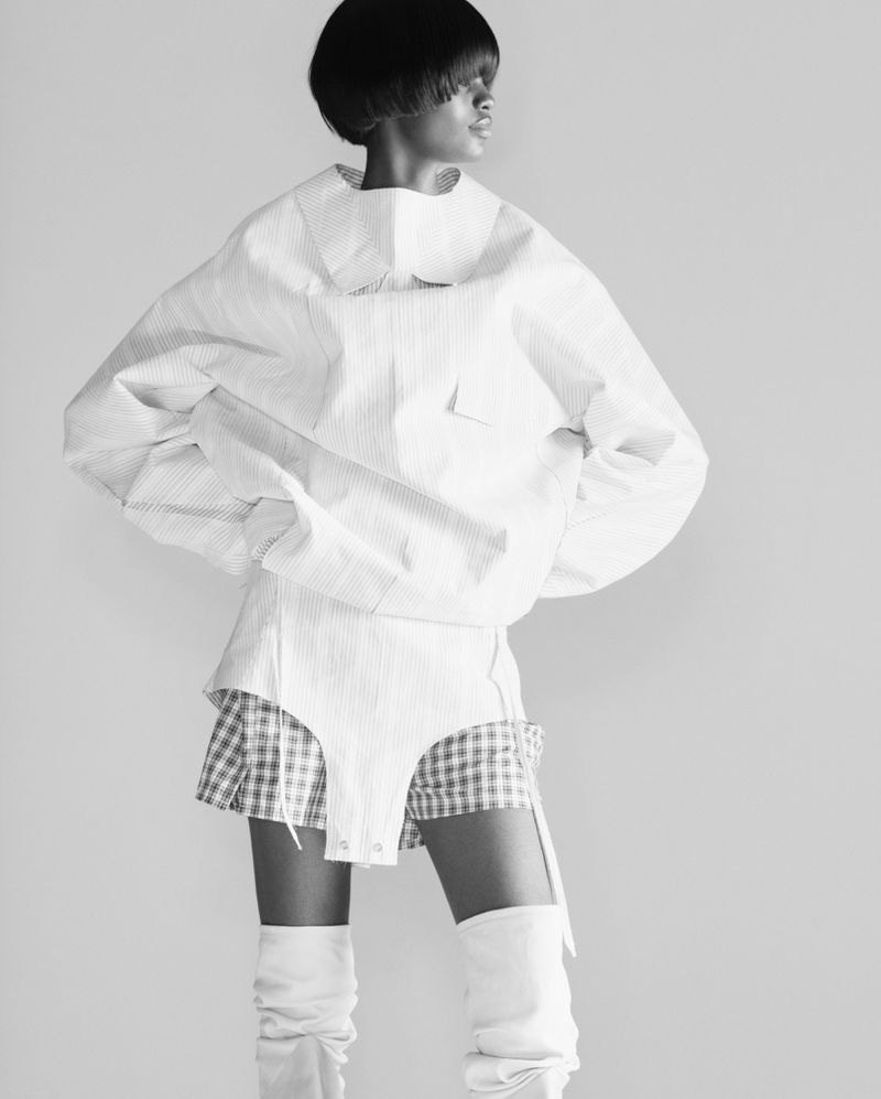 Fashion editorial shot in black and white featuring a Black female model in an oversized white top and checkered shorts.
