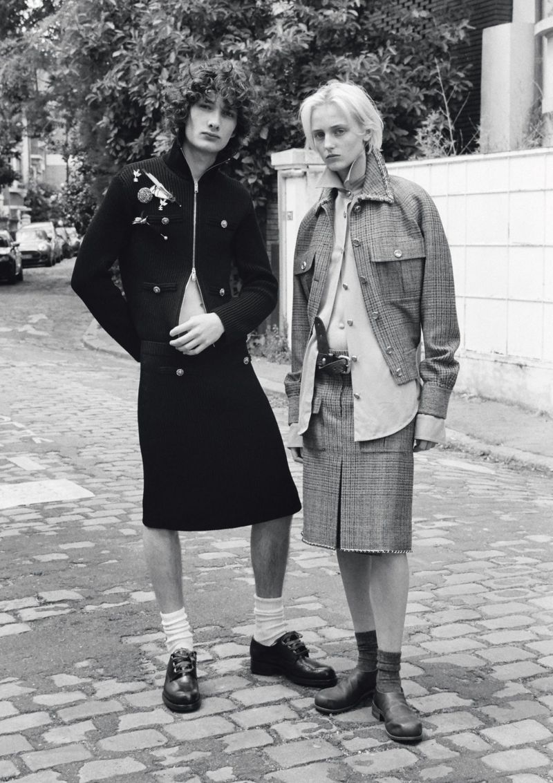 Black and white portrait of two models in tailored skirts and jackets standing on a cobblestone street.