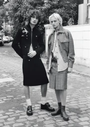 Black and white portrait of two models in tailored skirts and jackets standing on a cobblestone street.