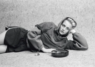 Model lying down on a textured surface wearing an oversized hoodie and athletic shorts next to an ashtray.