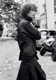 Model George Anderson in dark outerwear and pinstripe tailoring on a cobblestone street in black and white.