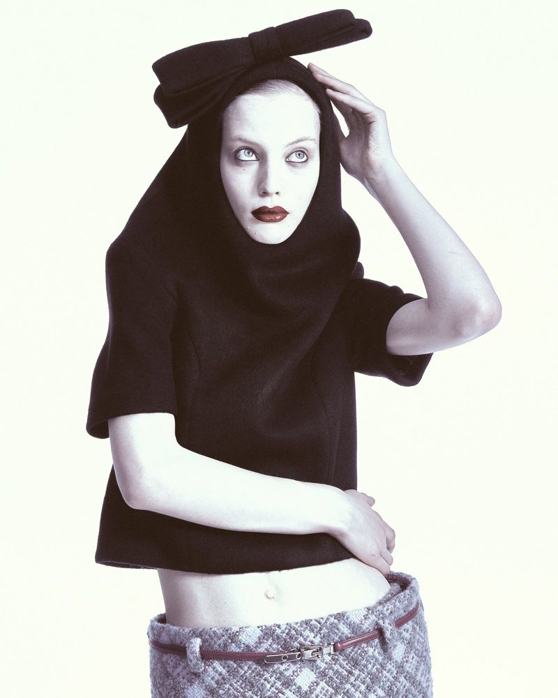 Model wearing a black hooded top with a large bow and tweed skirt against a white background