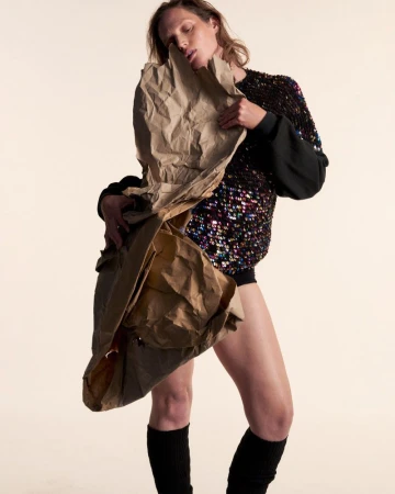 Model Vivien Solari holding a large sheet of crumpled brown paper wearing a sequin top against a studio background.