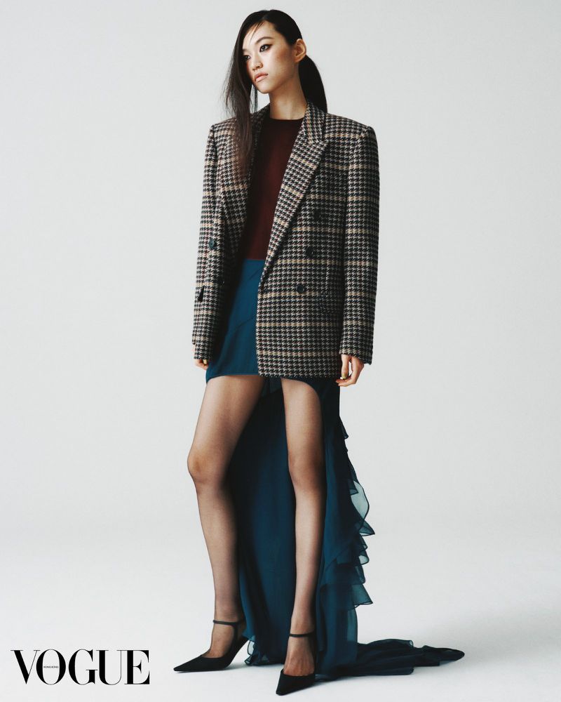Fashion editorial shot of an Asian woman in a blazer and dress, posing against a clean white background in a photo studio.