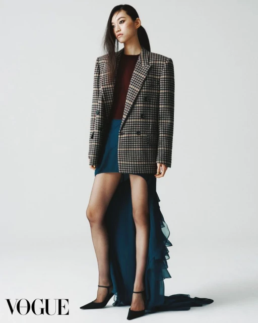 Fashion editorial shot of an Asian woman in a blazer and dress, posing against a clean white background in a photo studio.