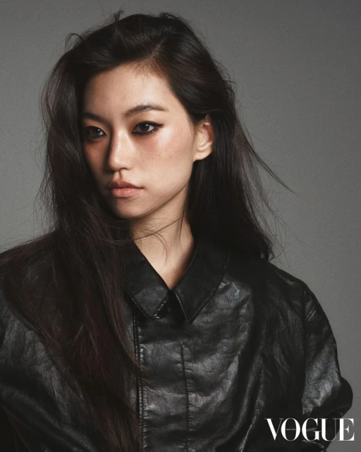 Close-up studio shot of an Asian woman wearing a black leather jacket against a grey backdrop with the Vogue logo in the corner.