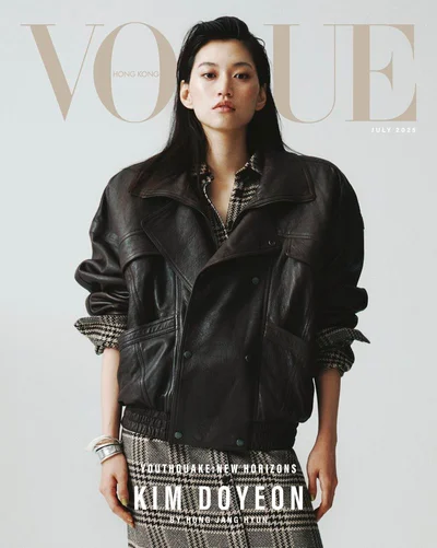 Kim Doyeon posing on the Vogue Hong Kong magazine cover wearing an oversized black leather jacket and plaid skirt against a pale backdrop.