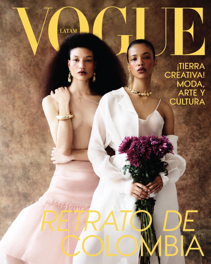 Two female models posing for Vogue Latin America July 2026 cover, holding purple flowers against a textured brown background