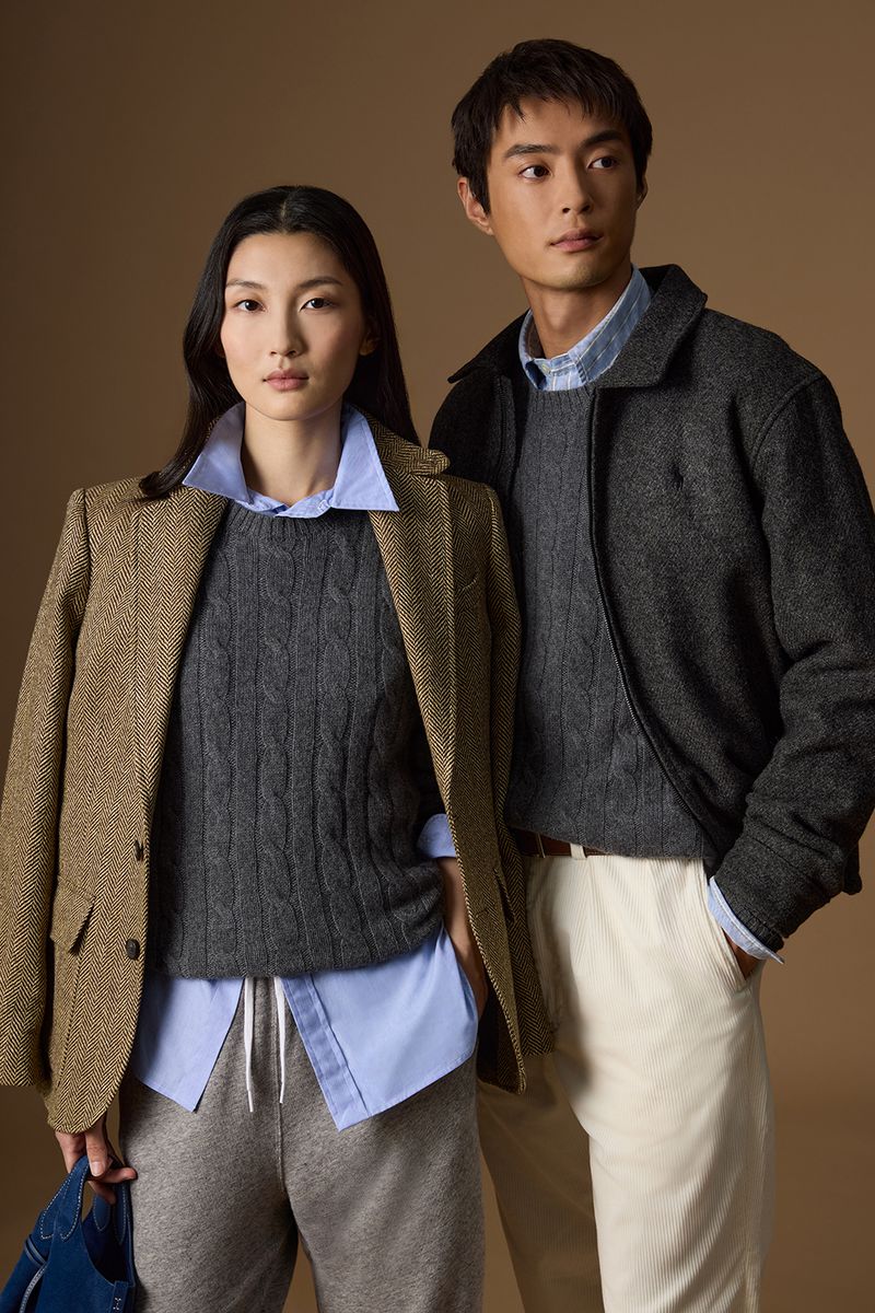 Two models in layered Polo Ralph Lauren knitwear, blazers, and collared shirts standing against a warm studio backdrop.