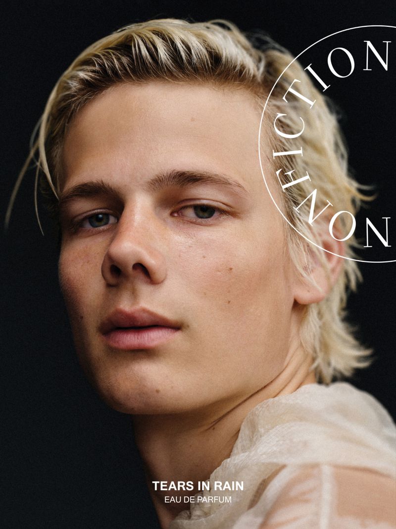 Close-up portrait of model Blue River Wild with blonde hair against a black background for a fragrance campaign.