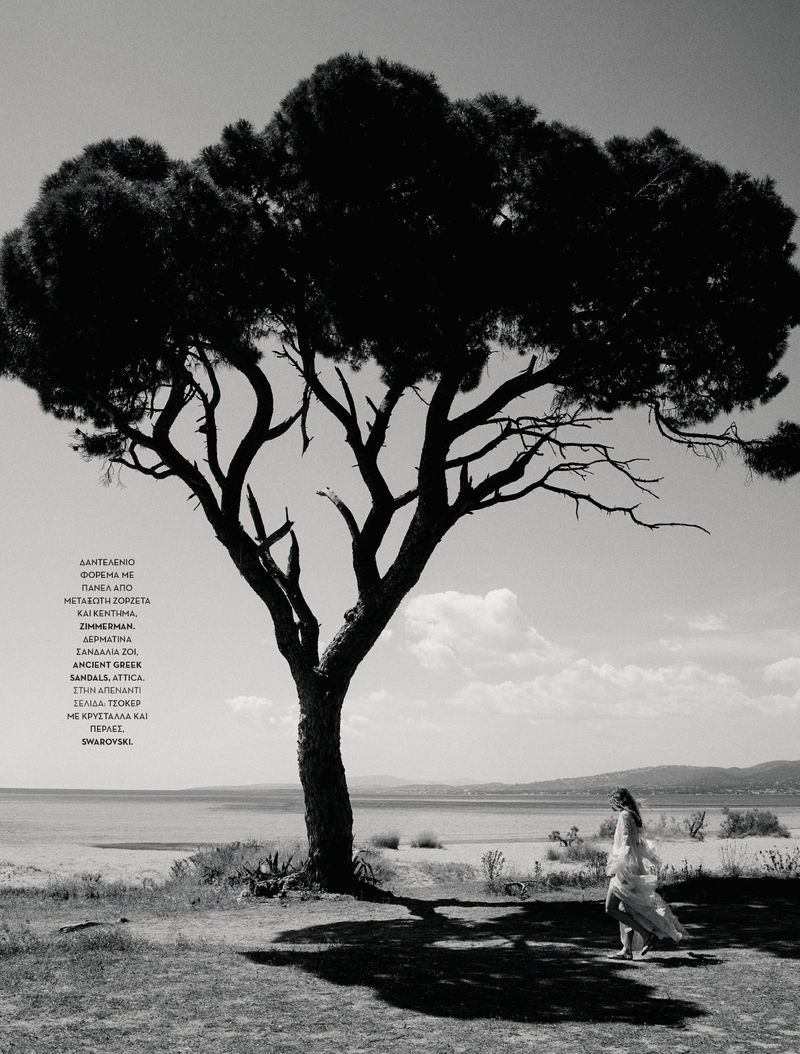 Black and white photograph of model Sabine Glud walking in a flowing dress beneath a large pine tree by the coast.