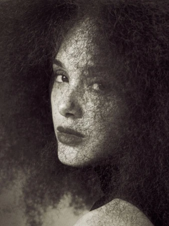 Close-up portrait of a woman with voluminous textured hair casting fine shadows across her freckled face in monochrome.