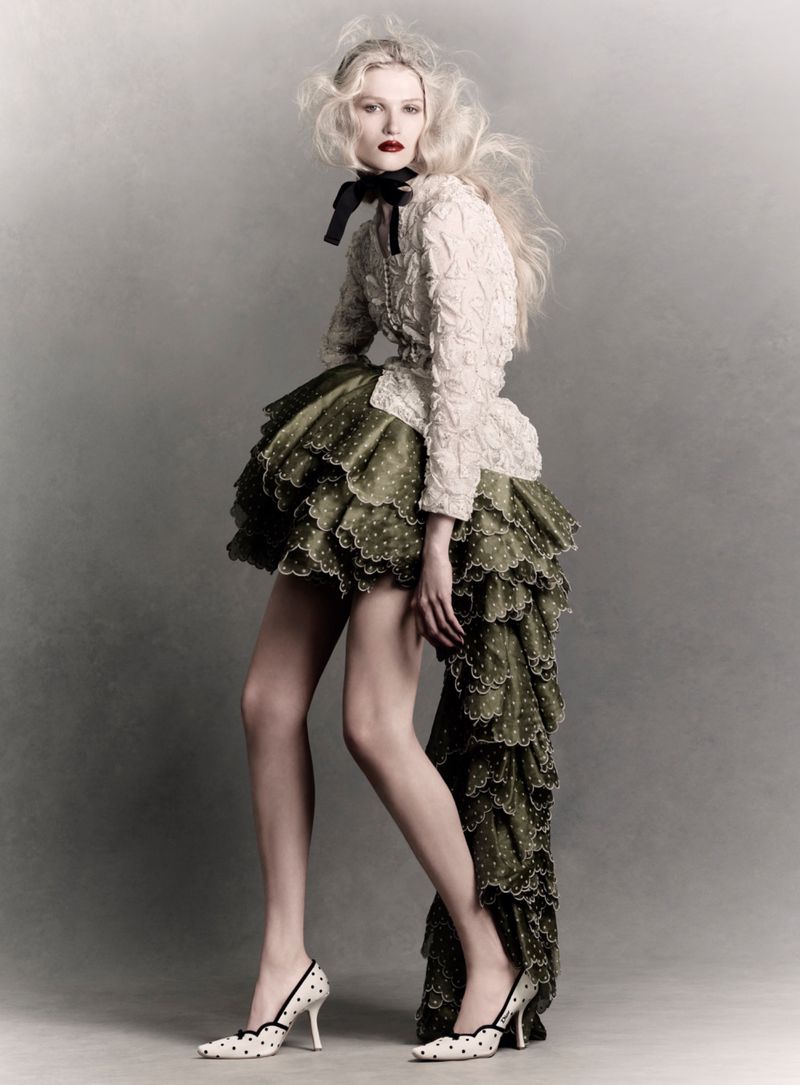 Model in textured cream top and voluminous green ruffled skirt against a grey background